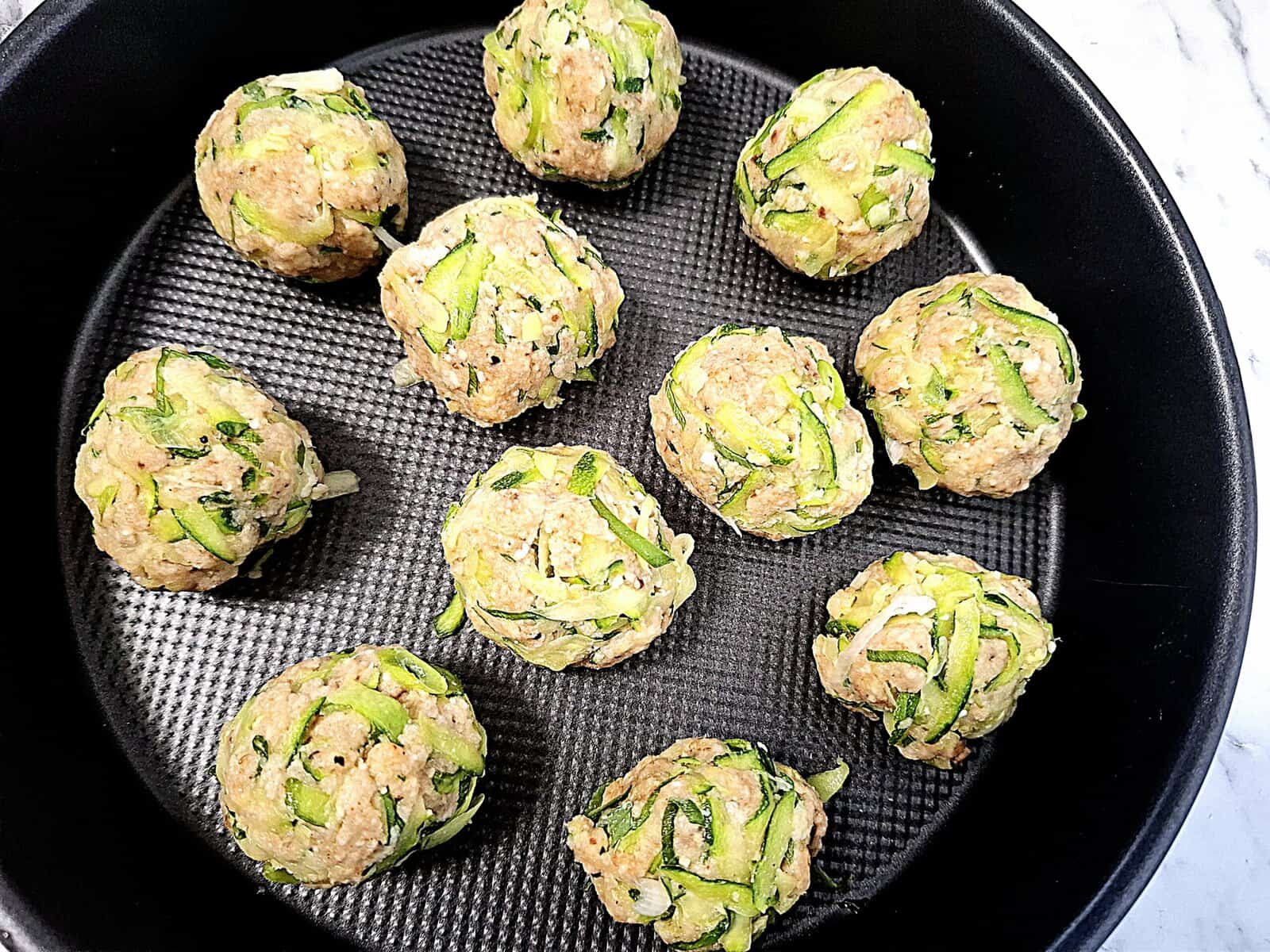 Uncooked zucchini balls on a round baking tray