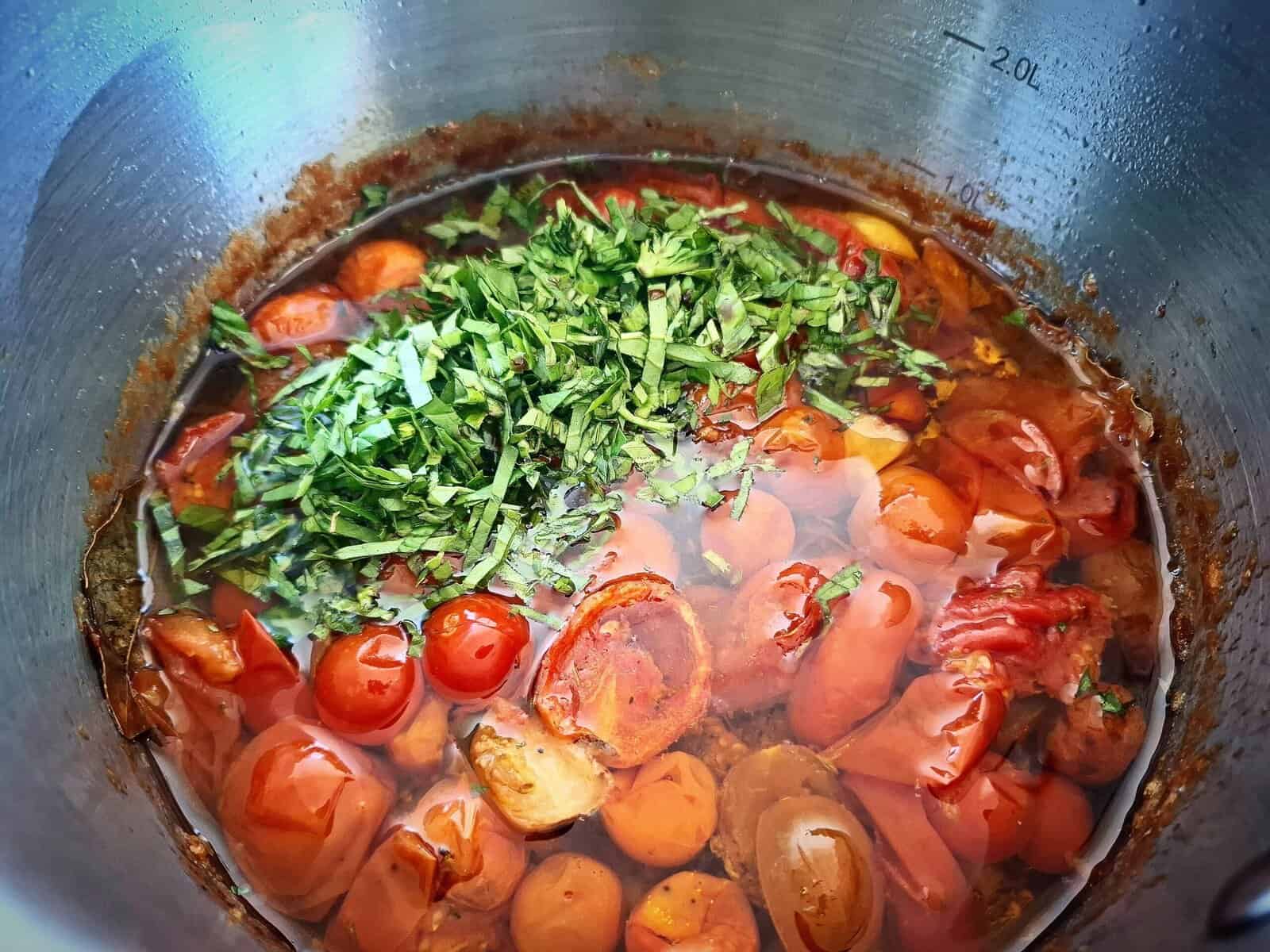 Sliced fresh basil leaves has been added to and sitting on top of tomato confit in a sauce pan