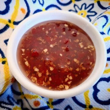 Candied chili in a white ramekin on a blue, yellow and white tea towel