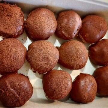 Twelve chocolate truffle cake ball dusted with cocoa powder in a recycled take away container
