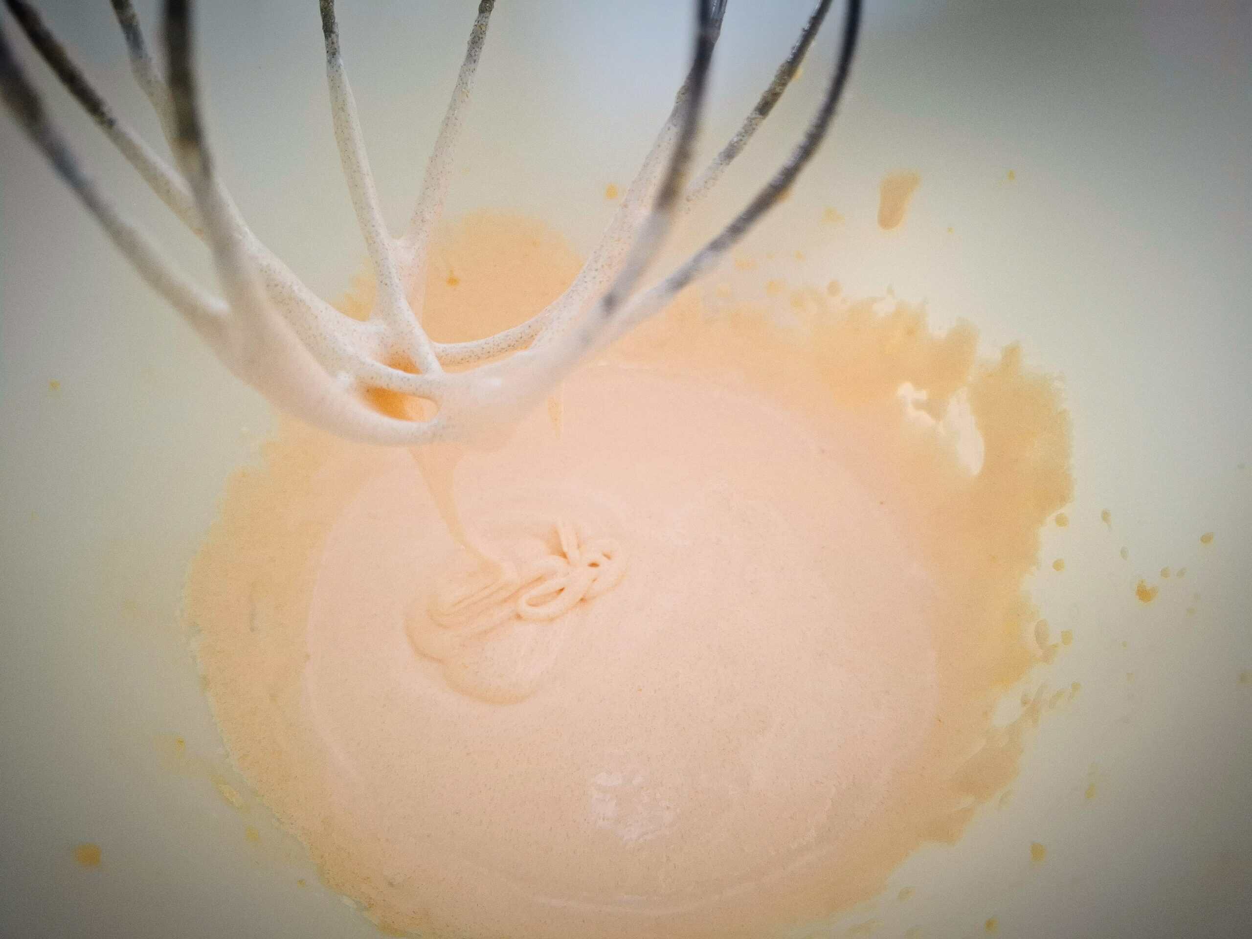 Egg yolks and sugar has been whipped pale and fluffy in a white kitchen mixer bowl with a whisk attachment