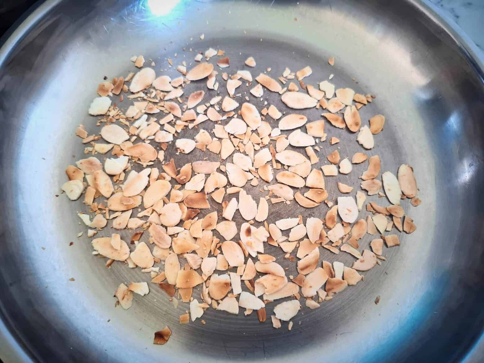 Roasting sliced almonds in a stainless steel frying pan.