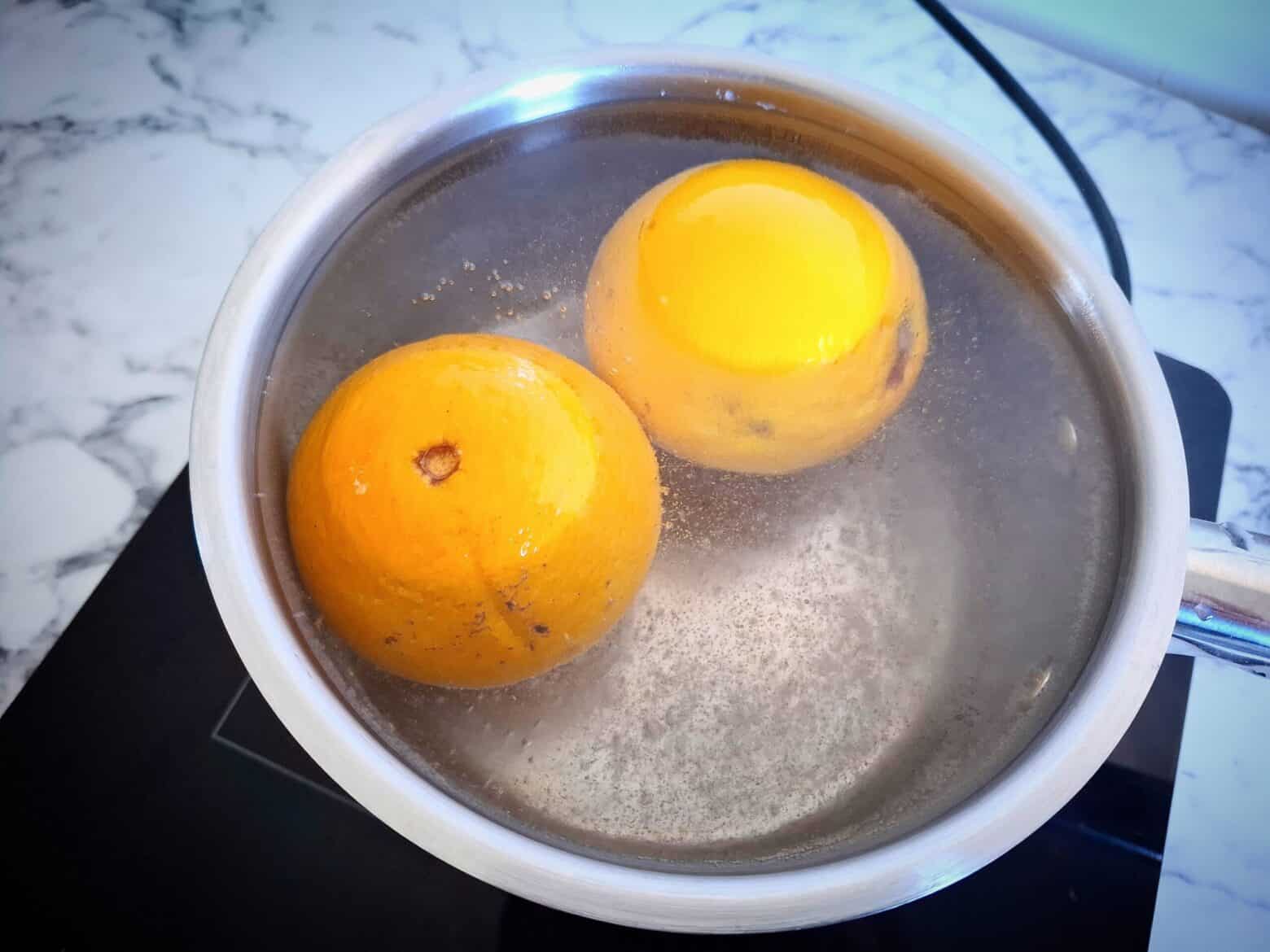 Two whole oranges submerged in water simmering in a saucepan.