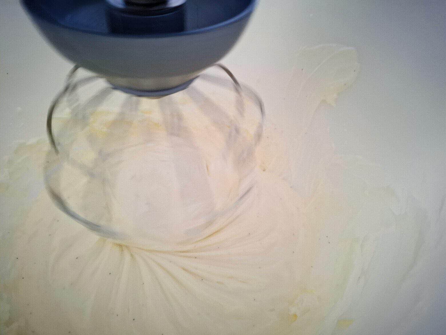 The greek yogurt icing is being mixed in a white kitchen mixer.