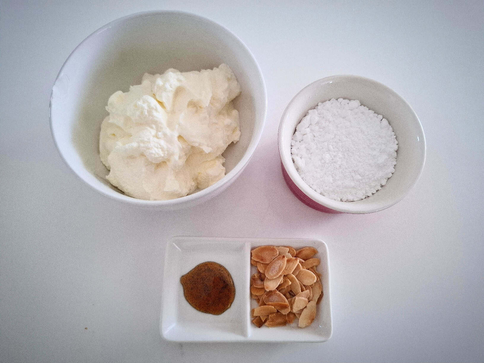 Ingredients for vanilla and Greek yogurt icing in ramekins on a marbled table top.