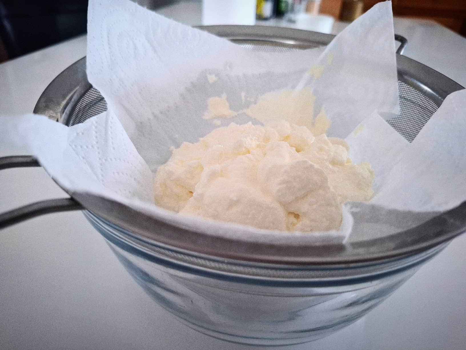 Greek yogurt in a fine strainer lined with a paper towel over a glass bowl