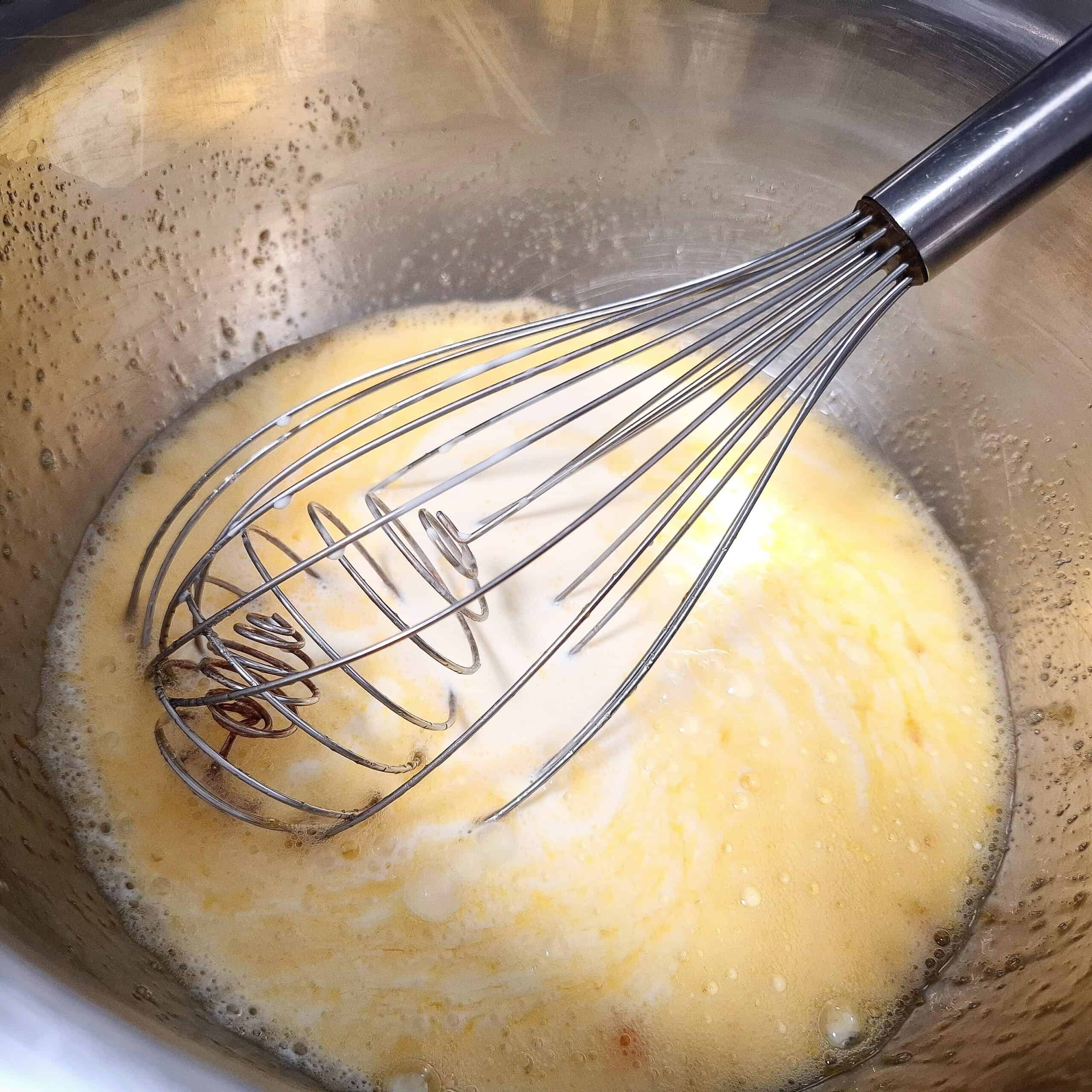 Whisking eggs, sugar and cream together with a balloon whisk in a stainless steel bowl