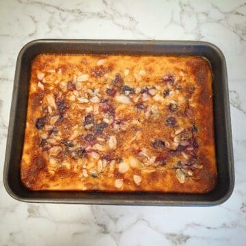 Blueberry baked custard with sliced almonds in a black rectangular baking tray on a marbled bench top.