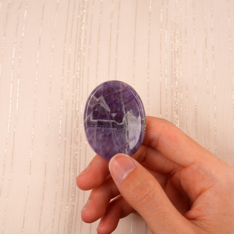 Fingers gently holding the Dream Amethyst stone, showing size and pattern
