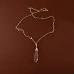 Handmade clear quartz point pendant on light neutral or white background