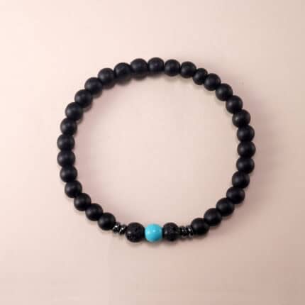 Matte black obsidian and turquoise beaded bracelet on plain background with silver charm