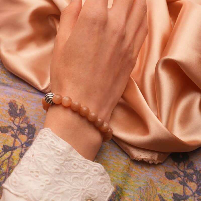 Worn by a relaxed hand in natural lighting, highlighting the soft peach tones and peaceful aura