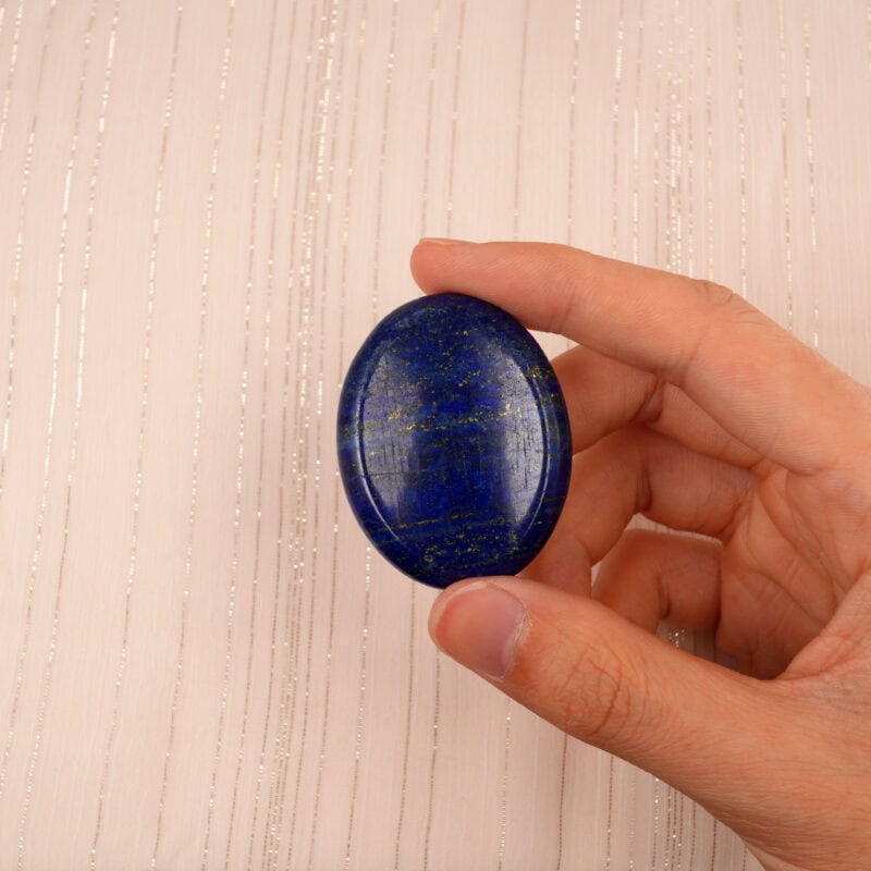 Hand holding a Lapis Lazuli worry stone between fingers, showing size and texture