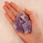 Hand holding a raw Amethyst stone, emphasizing its vibrant purple color and rough, unpolished surface.