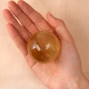 Hand holding a glowing Citrine crystal ball, showing size and warmth