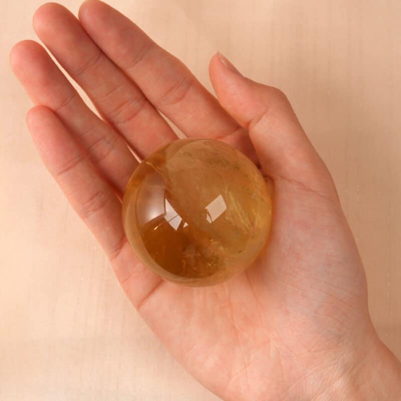 Hand holding a glowing Citrine crystal ball, showing size and warmth
