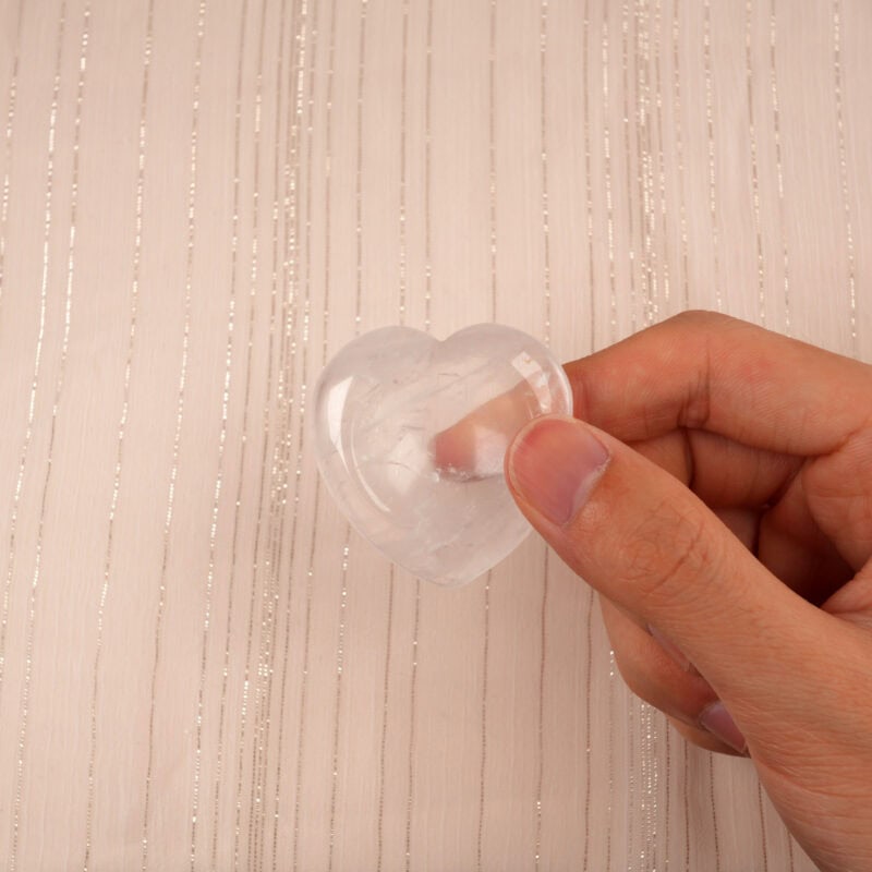 Hand holding a transparent clear quartz heart crystal to show its size and clarity