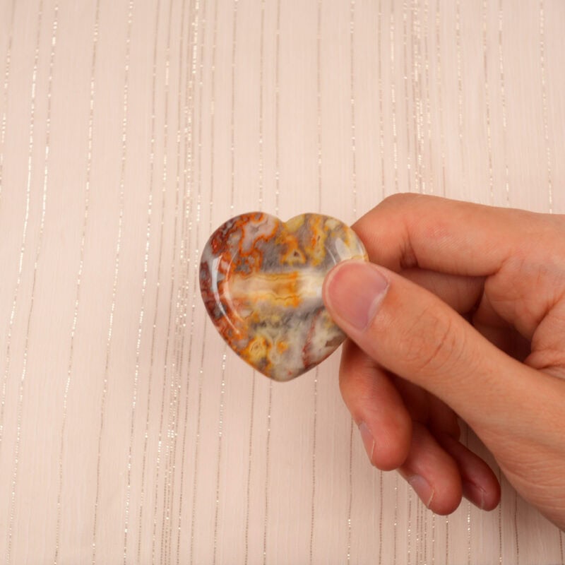 Fingers gently holding a Crazy Lace Agate heart-shaped worry stone