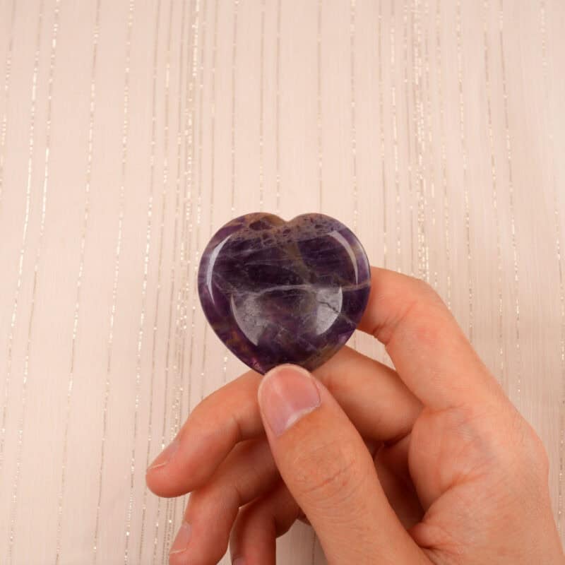 Hand gently holding a Dream Amethyst heart-shaped worry stone between fingers