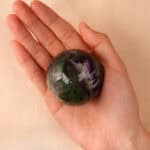 Hand holding the Feather Fluorite sphere, showing transparency and size