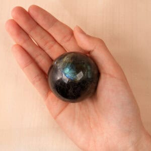Hand holding labradorite sphere to show size and flash effect