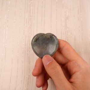 Fingers holding a polished labradorite heart worry stone, highlighting its size and glow