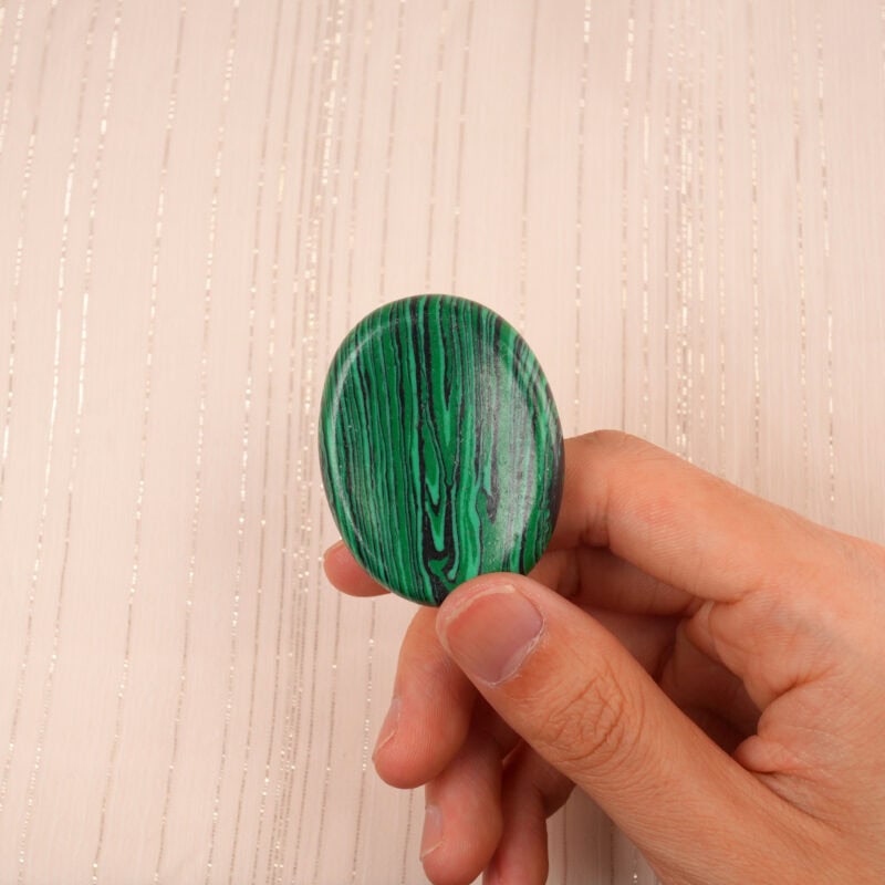Hand gently holding a Malachite worry stone, showcasing its size and intricate details