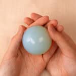 Fingers gently holding a glowing opal sphere, highlighting its shimmer and size