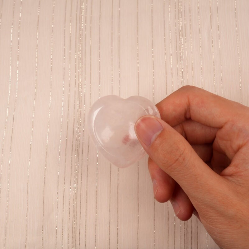 Fingers gently pinching a small Rose Quartz heart crystal against a neutral background
