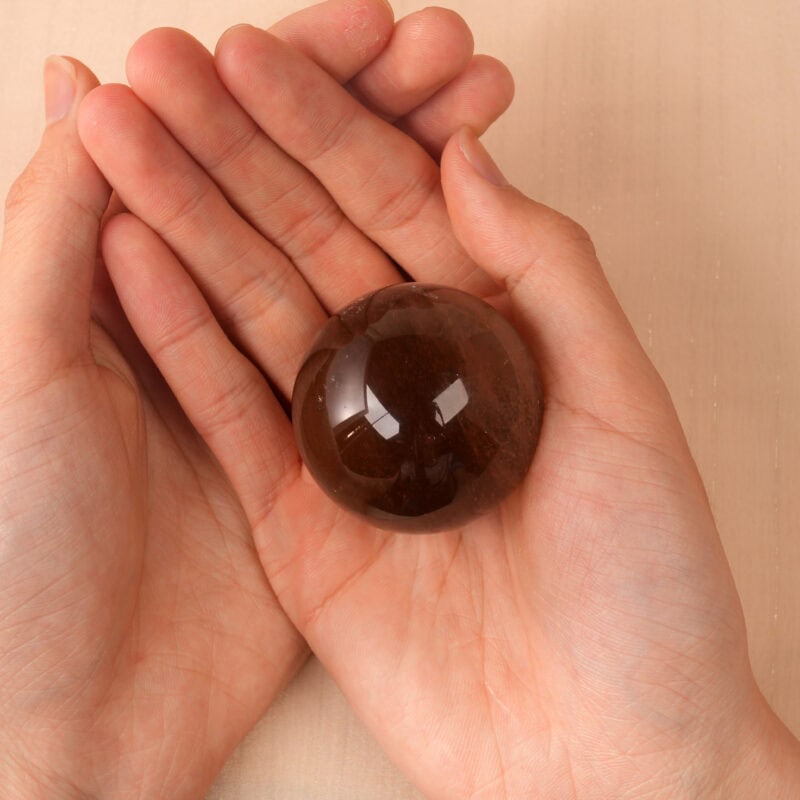 Hand holding the Smoky Quartz sphere, showing its size and clarity