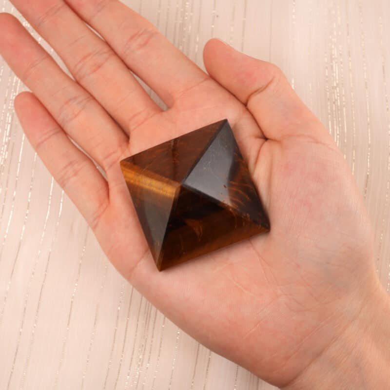 Hand holding a natural tiger eye pyramid, used as a good luck charm and energy focus crystal
