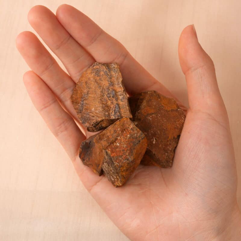 Hand holding a piece of Tiger Eye raw stone, highlighting its shimmer and layered surface.