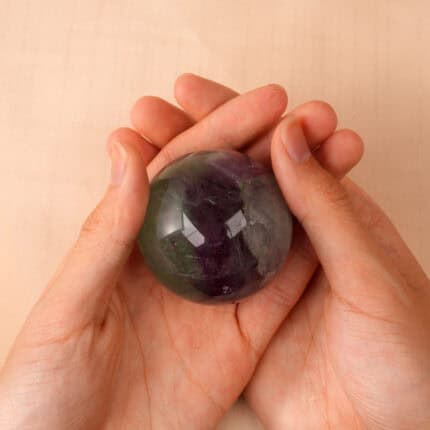 Hand holding the sphere to show size, smoothness, and vibrant hues