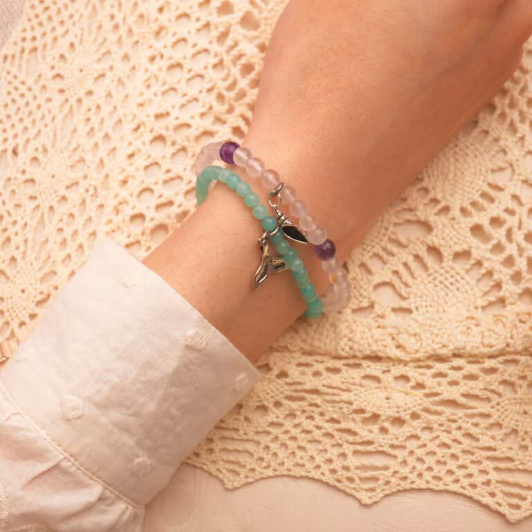 Model wearing layered gemstone bracelets in soft tones.