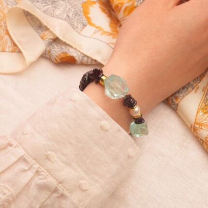 The bracelet worn on the wrist, showing a stylish combination of garnet, pearl, and aquamarine stones.