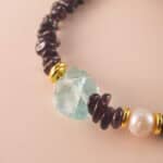 Close-up of polished garnet, lustrous pearl, and translucent aquamarine beads strung on durable elastic cord.