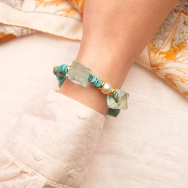 Wrist wearing a turquoise, pearl, and aquamarine Taurus bracelet in soft light.