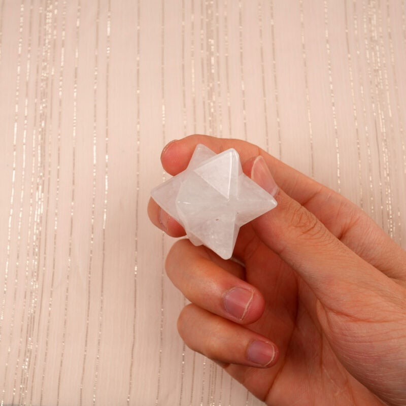 Clear quartz Merkaba ornament held in hand, showing its transparency and detailed carving.