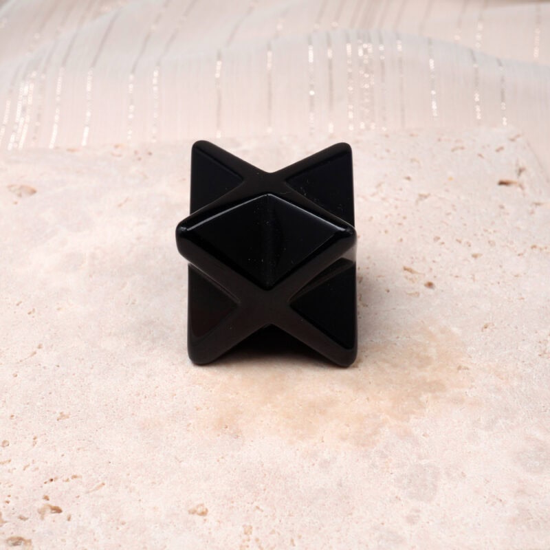 Polished Obsidian Merkaba crystal ornament on a beige stone background.