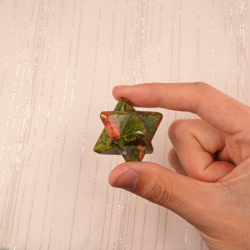 A hand holding the Unakite Merkaba crystal, highlighting its green-pink tones