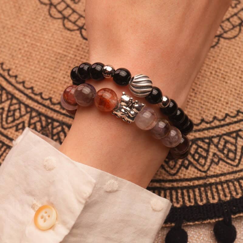 Model wearing stacked bracelets in deep black and light purple hues.