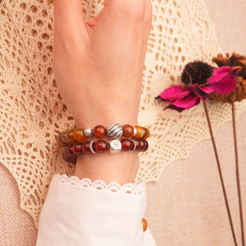 Model wearing stacked gemstone bracelets in warm red hues.