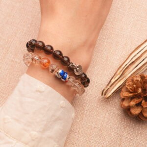 Model wearing stacked smoky quartz and rutilated quartz bracelets on wrist.