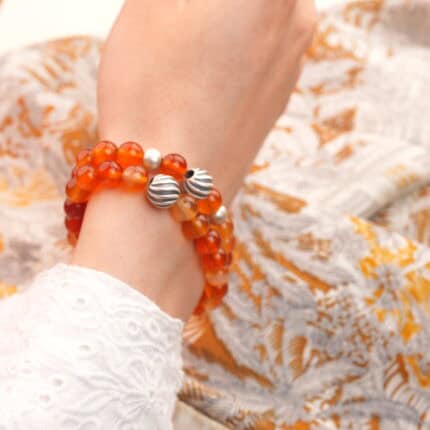 Model wearing two flower red agate bracelets stacked on wrist.