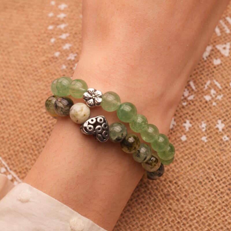 Model wearing stacked green-toned gemstone bracelets.