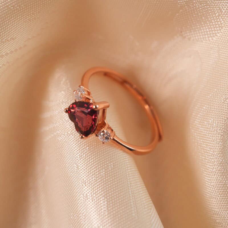 Adjustable rose gold ring with a heart-shaped garnet centerpiece, displayed on a clean white background.