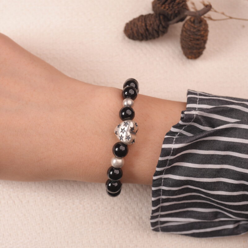 Lifestyle shot of the black obsidian and aquamarine bracelet worn on the wrist, showcasing its elegant design and delicate silver heart charm.