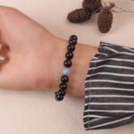 Lifestyle shot of the black obsidian and aquamarine bracelet worn on the wrist, showcasing its elegant design and delicate silver heart charm.
