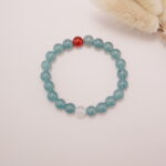 The Green Aventurine and Red Agate bracelet laid on a soft surface, highlighting its calming green hues with the bold red and white accents, creating a serene yet energetic atmosphere.