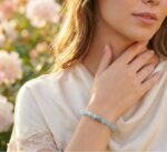 A woman gently touching her neck while wearing a crystal bracelet outdoors, expressing a soft and elegant lifestyle.